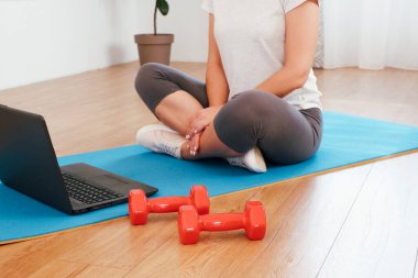 Laptopla ev çalışması ve ev konsepti. Spor salonundaki kadın dizüstü bilgisayarda ders izliyor ve içeride spor yaparken spor yapıyor. Beyaz tenli kadın evde online fitness dersi alıyor..