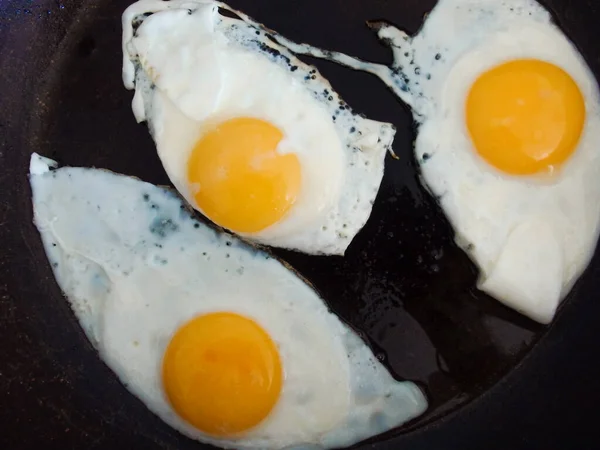 三个煎蛋 用橄榄油在锅里煎 把三个鸡蛋放在锅里煎 黑色背景 — 图库照片