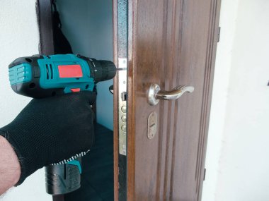 Usta işçi ön kapıya bir kapı kilidi takıyor, polimer kaplamalı metal kapılar, elektrikli matkap tornavida, yakın çekim..