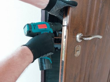 Usta işçi ön kapıya bir kapı kilidi takıyor, polimer kaplamalı metal kapılar, elektrikli matkap tornavida, yakın çekim..