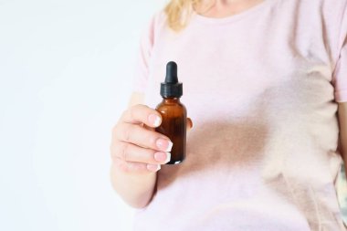 Woman's hand hold natural skincare serum in dropper bottle on white background . Cosmetic beauty background. Concept of body care, rejuvenation.