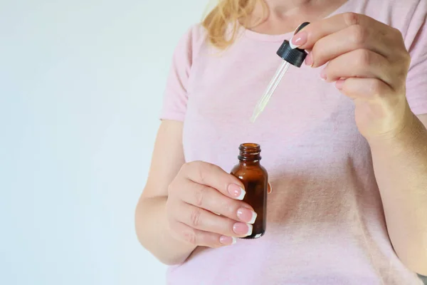 Woman's hand hold natural skincare serum in dropper bottle on white background . Cosmetic beauty background. Concept of body care, rejuvenation.