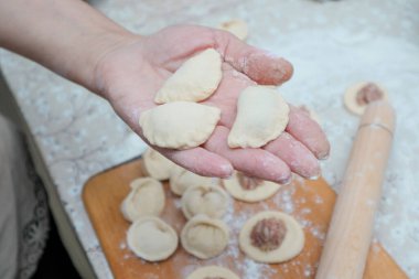 Raw homemade dumpling with meat in hands of housewife. Making process of convenience food. Raw dough