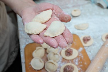Raw homemade dumpling with meat in hands of housewife. Making process of convenience food. Raw dough