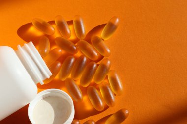 Omega 3 'ün şişe kapsüllerinden dökülüyor, yakın plan fotoğraf, turuncu arka plan. Balık yağı kapsülleri şişeden dökülüyor.