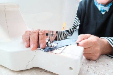 Elle dikiş makinesinin görüntüsü. Yaşlı bir erkek terzi elektrikli dikiş makinesine dikiş diker. Ellere yakın çekim.