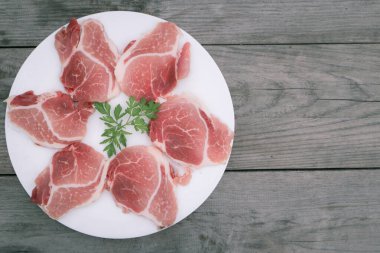 Beyaz yuvarlak tabakta çiğ domuz dilimi Eski ahşap masa üzerinde.