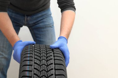 Beyaz arka planda siyah bir lastiği iten tamirci elleri. Lastik tutan bir adam. Kış ve yaz lastiklerinin değiştirilmesi.