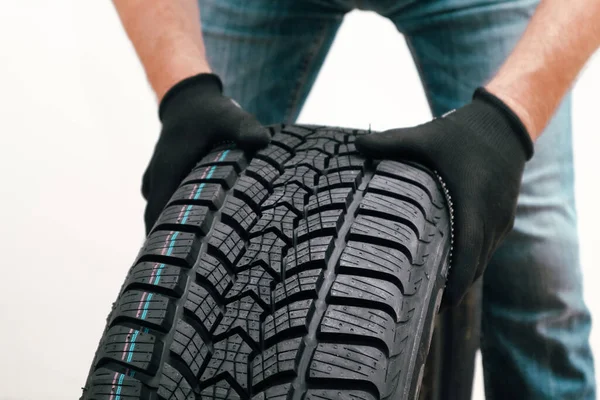 Closeup of mechanic hands pushing a black tire on a white background. Man holding a tire. Replacement of winter and summer tires.