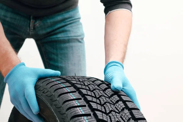 Closeup of mechanic hands pushing a black tire on a white background. Man holding a tire. Replacement of winter and summer tires.