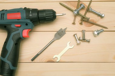Ahşap masadaki aletler, matkap uçları ve cıvatalı vidaları olan elektrikli bir tornavida. Diy konsepti. Ekipman, iş yeri. Düz konum.