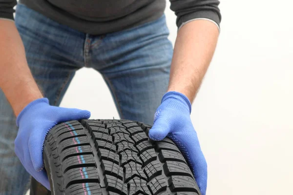 Closeup of mechanic hands pushing a black tire on a white background. Man holding a tire. Replacement of winter and summer tires.