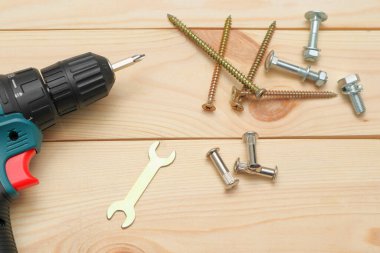 Ahşap masadaki aletler, matkap uçları ve cıvatalı vidaları olan elektrikli bir tornavida. Diy konsepti. Ekipman, iş yeri. Düz konum.