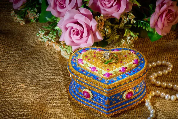 the beautiful box is shot on a brown cloth background with a necklace of pearls and pink flowers , can be used as a greeting card