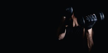 Genç adam dambıllarla kas ve güç egzersizleri yapıyor. Yüksek yoğunluklu fitness. Uzayı kopyala Seçici odak.