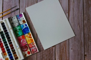 Bir palet suluboya boya, boş kağıt ve ahşap arka planda fırçalar. Sanatçının çalışma alanı. Uzayı kopyala Seçici odak.