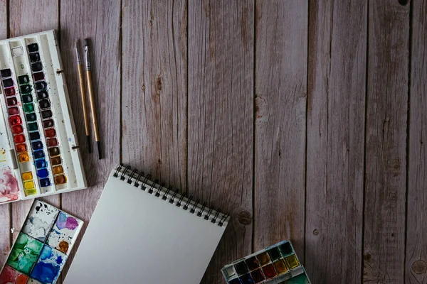 Bir palet suluboya boya, boş kağıt ve ahşap arka planda fırçalar. Sanatçının çalışma alanı. Uzayı kopyala Seçici odak.