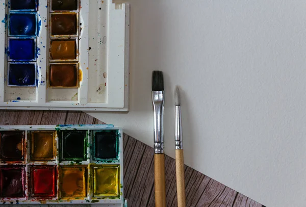 Bir palet suluboya boya, boş kağıt ve ahşap arka planda fırçalar. Sanatçının çalışma alanı. Uzayı kopyala Seçici odak.