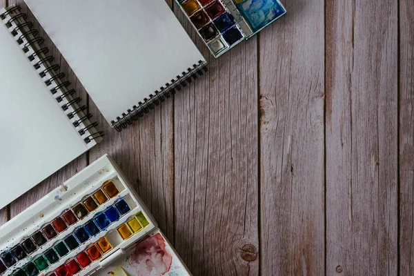 Bir palet suluboya boya, boş kağıt ve ahşap arka planda fırçalar. Sanatçının çalışma alanı. Uzayı kopyala Seçici odak.