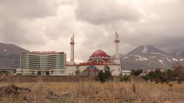 Erzurum, Türkiye 'de 05.01.01.2021 Erzurum Hastanesi' nde, arka planda bir caminin yanında Nisan ayı sonunda karla kaplı bir dağ bulunmaktadır. Türkçe: Erzurum sehir hastanesi ve Darl fun camii