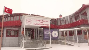 Türkiye 'de kar fırtınası sırasında Erzurum. Aile sağlığı merkezine kar yağıyor (Türkçe: Aile merkezi) Balkondaki büyük çatı buzları. Kış, kar fırtınası, kartopu. Donmuş, buz