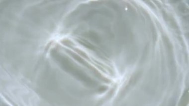 Su sıçraması. Su damlası dalgalanma yaratıyor. Güneş ışığını yavaş çekimde yansıtan saf su. Su yüzeyi üst görünümü. Temiz yüzme havuzu dalgalanmaları ve el sallamalar. 4k