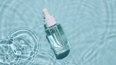 Pipetli cam kozmetik şişesi suyun yüzeyinde yatıyor. Su manzarası mavi renkte. Saf mavi su, güneş ışığı yansıtıyor. Tasarım için ambalaj örneği, reklam 45 'liği