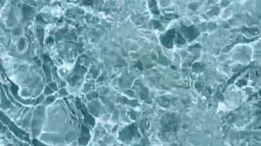 Su yüzeyi üst görünümü. Su mavi renklidir. Saf mavi su, güneş ışığını yavaş çekimde yansıtıyor. Güneş ve gölgeler. Hareket temiz yüzme havuzu dalgalanmaları ve el sallama. 4k