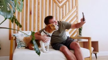 Masada oturan neşeli genç bir adam ve evcil hayvanla telefon kullanarak selfie çekiyor. Mans en iyi arkadaş. Yavaş Hareket.