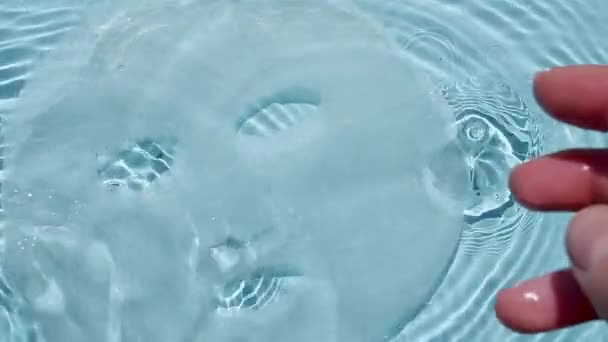 Косметична маска для догляду за шкірою на поверхні води. Вид зверху повільний рух хвиль води і падаючих крапель води, краплі дощу. Прозора блакитна вода з відбиттям, заломленням сонячного світла і тінями . — стокове відео