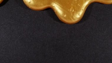 Mikro baloncuklu altın sıvı jel siyah yüzeyde yavaşça kayıyor. Makro Vuruş