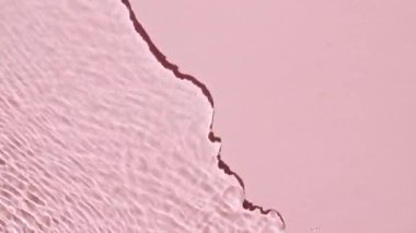 Su yüzeyi üst görünümü. Su pembe renkte sıçrıyor. Saf mavi su, güneş ışığını yavaş çekimde yansıtıyor. Hareket temiz yüzme havuzu dalgalanmaları ve el sallama. 4k