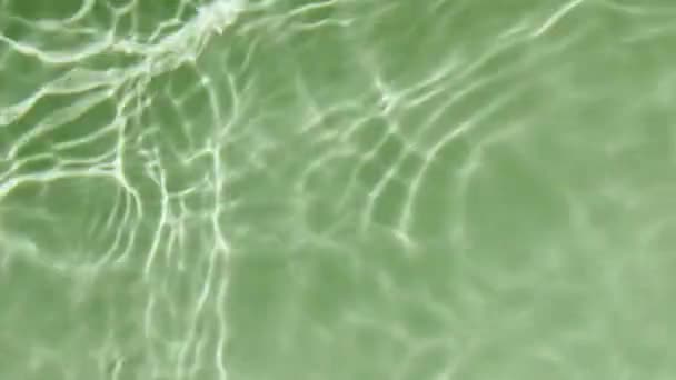 Eau éclaboussure de couleur verte. Goutte tombe dans l'eau et les cercles divergents de l'eau sur fond vert. Eau pure avec reflets ensoleillés au ralenti. Des ombres. Ondulation propre de la piscine et vague — Video