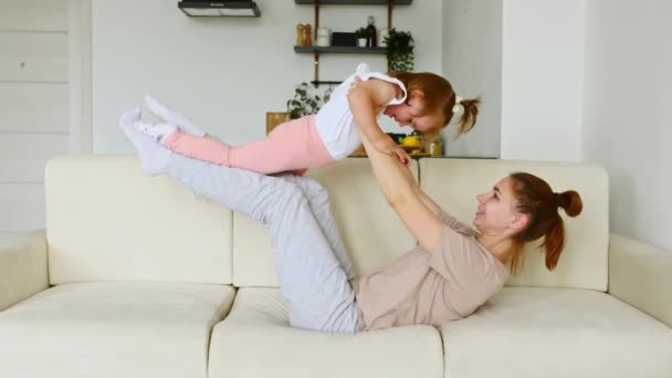 Mãe feliz e filha pequena rindo se divertindo deitada no sofá e brincando. Família mãe com diversão infantil brincando juntos em casa. — Vídeo de Stock