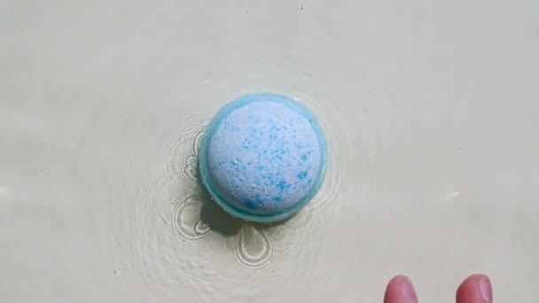 Bola azul bomba de baño se disuelve en agua con burbujas de espuma blanca. Producto cosmético natural y cuidado de la piel. Agua clara con reflejos, refracción de la luz solar y sombras. — Vídeos de Stock