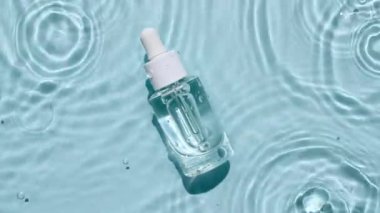 Pipetli cam kozmetik şişesi suyun yüzeyinde yatıyor. Su manzarası mavi renkte. Saf mavi su, güneş ışığı yansıtıyor. Tasarım için ambalaj örneği, reklam 45 'liği