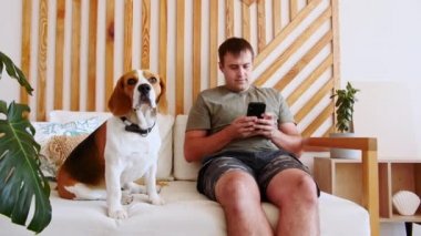 Neşeli genç bir adam masada oturmuş video görüşmesi yaparken köpeğine sarılıyor. Köpeğin sahibi evcil hayvanla birlikte telefon kullanarak selfie çekiyor. Yavaş Hareket.