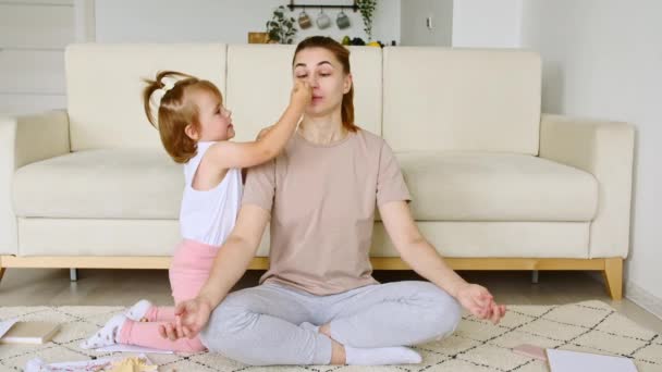 Mamma che fa esercizio yoga a casa per alleviare lo stress rilassante, mentre la sua bambina piccola figlia distrae e attira l'attenzione. Rallentatore — Video Stock