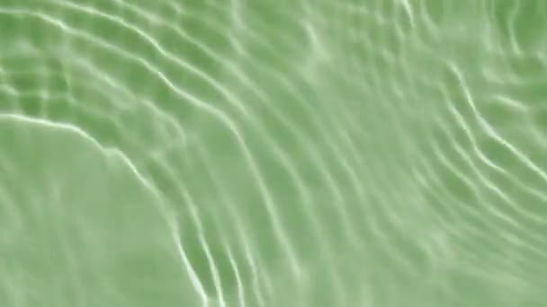 Air memercikkan warna hijau. Drop jatuh ke dalam air dan menyimpang lingkaran air di latar belakang hijau. Air murni dengan pantulan sinar matahari dalam gerakan lambat. Kolam renang bersih riak dan gelombang. 4k — Stok Video