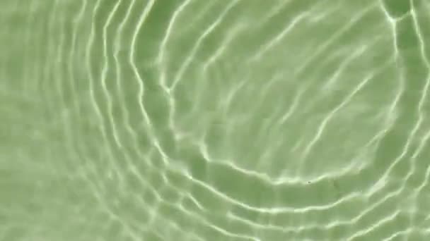 Eau éclaboussure de couleur verte. Goutte tombe dans l'eau et les cercles divergents de l'eau sur fond vert. Eau pure avec reflets ensoleillés au ralenti. Propre ondulations de piscine et vague. 4k — Video