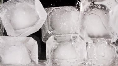 Suda buz küpleri ve siyah arka planda hava kabarcıkları. Buzlu bardağa su dökmek. Yavaş çekim.