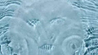Su yüzeyindeki cilt bakımı için kozmetik ve yüz maskesi. Üst görüntü dalgaların yavaş çekimi su damlaları, yağmur damlaları. Yansımalı berrak mavi su, kırılma güneş ışığı ve gölgeler..