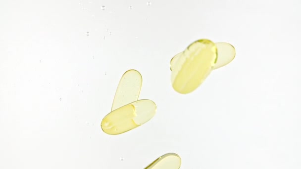 Prášky na kapsle, kapsle zlatého oleje Omega3. Makro záběr pilulky padající do vody a vzduchové bubliny na bílém pozadí. Koncept medicíny, zdravotní péče, léčba. Zpomalený pohyb. — Stock video