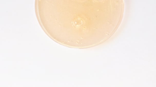 Crema cosmética transparente amarilla del gel con las burbujas de la molécula que fluyen en la superficie blanca llana. Macro Shot — Vídeo de stock