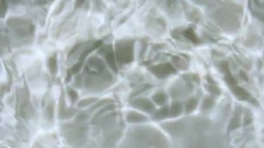 Su sıçraması. Su damlası dalgalanma yaratıyor. Güneş ışığını yavaş çekimde yansıtan saf su. Güneş ve gölgeler. Su yüzeyi üst görünümü. Temiz yüzme havuzu dalgalanmaları ve el sallamalar. 4k