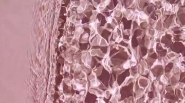 Saf pembe su, güneş ışığını yavaş çekimde yansıtıyor. Su yüzeyi üst görünümü. Güneş ve gölgeler. Hareket temiz yüzme havuzu dalgalanmaları ve dalga.