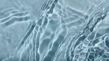 Su yüzeyi üst görünümü. Su mavi renklidir. Saf mavi su, güneş ışığını yavaş çekimde yansıtıyor. Güneş ve gölgeler. Hareket temiz yüzme havuzu dalgalanmaları ve el sallama. 4k