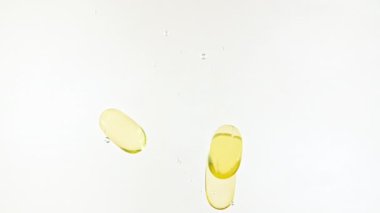 Kapsül hapları, Omega 3 altın yağ kapsülleri. Suya düşen hapların makro çekimi ve beyaz arka planda hava kabarcıkları. Tıp konsepti, sağlık, tedavi. Yavaş çekim.