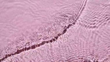 Saf pembe su, güneş ışığını yavaş çekimde yansıtıyor. Su yüzeyi üst görünümü. Hareket temiz yüzme havuzu dalgalanmaları ve dalga.