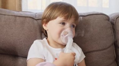 Maske takan küçük bir kız ciğerlerine duman ilacı soluyor. Çocuk evde astım spreyinden nefes alıyor.